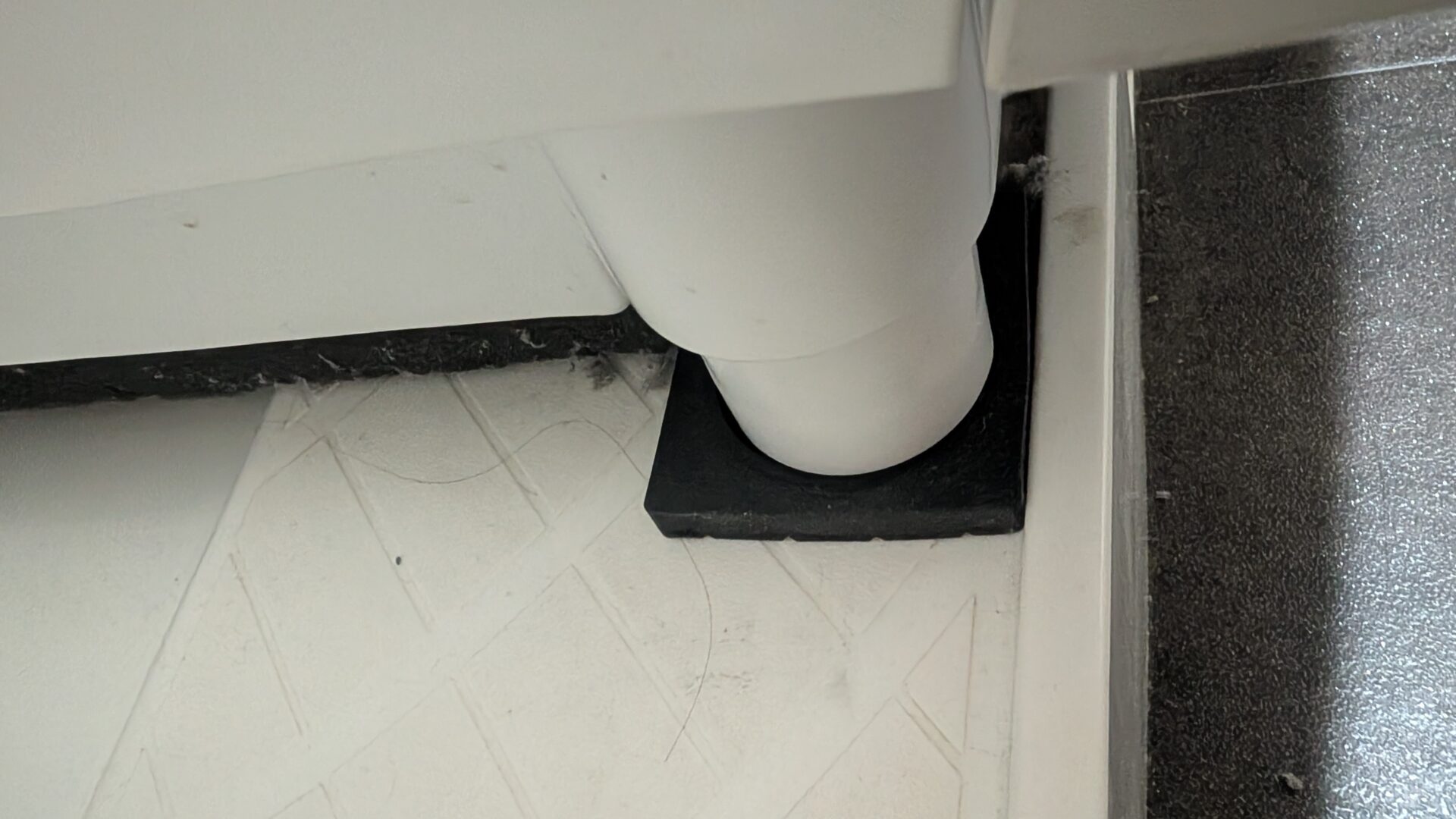 かさ上げ防水パンの上で、ドラム式洗濯機の脚の下に黒い防振ゴムを敷いている状態のアップ写真