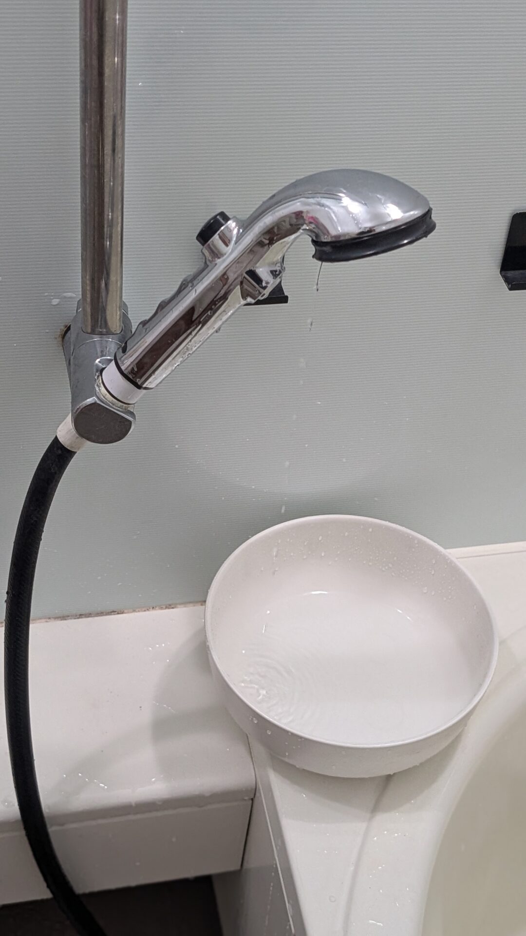 手元ストップを押した状態のシャワーヘッドから水が落ち、下に置いた洗面器に溜まっている