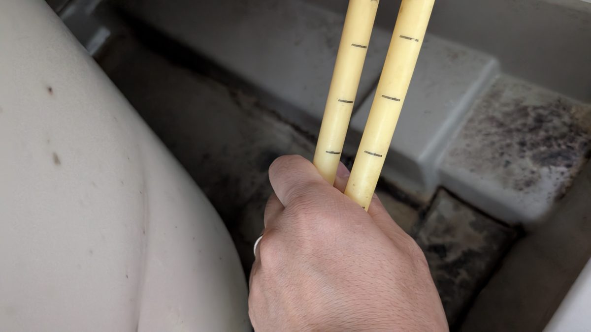 浴槽の裏を通る2本の黄色い管を手で持って見せているところ