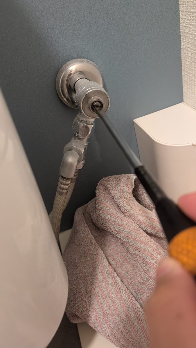 トイレの止水栓の溝にマイナスドライバーを当てて閉めているところ。下には床を濡らさないようにタオルが敷いてある